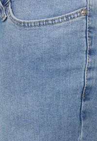 Calças de ganga azul-claro com uma leve textura, apresentando um botão prateado na cintura e detalhes em costura nos bolsos.