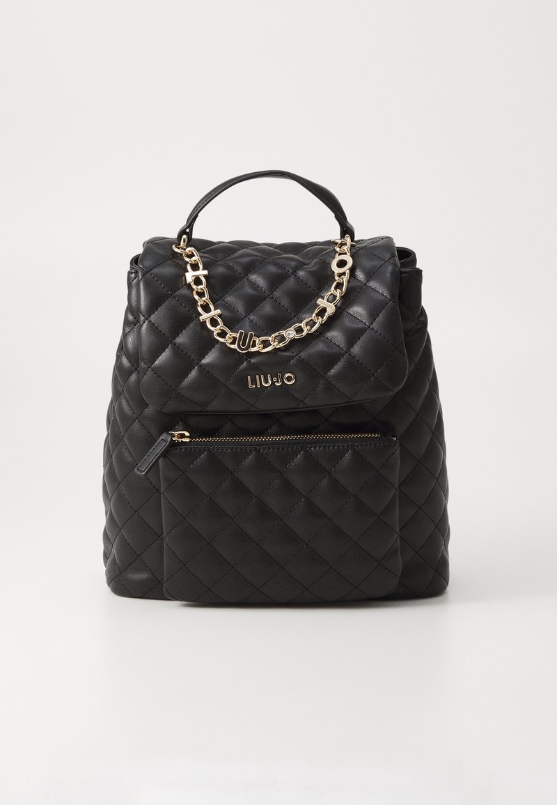 Mochila negra acolchada con un acento de cadena dorada, asa superior y bolsillo con cremallera frontal, con una textura de cuero suave. Nombre de la marca visible.
