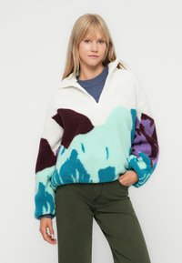 Pullover in pile con zip a metà, caratterizzato da una base bianca e motivi astratti multicolori in teal, viola e bordeaux. Vestibilità comoda.