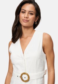 Robe sans manches en lin blanc avec un décolleté en V profond, taille cintrée et une grande boucle en bois. Texture lisse, design minimaliste.