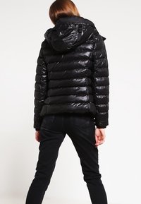 Czarna kurtka puchowa o błyszczącej powierzchni, pikowane wzornictwo, odpinany kaptur i elastyczne mankiety, w połączeniu z ciemnymi dżinsami.