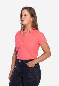 Koraalroze polo shirt met korte mouwen, voorzien van een knoopsluiting en een klein logo. Gecombineerd met high-waisted zwarte denim jeans.