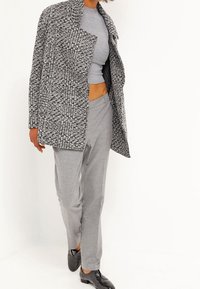 Kabát z vlněné směsi v černobílém károvaném vzoru s klopovým límcem, přes šedý žebrovaný crop top a odpovídající šedé kalhoty, doplněný černými botami.