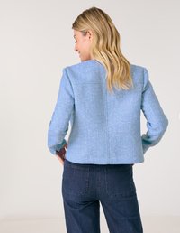 Hellblauer Tweed-Blazer mit strukturiertem Finish, definierten Schultern und verkürztem Schnitt, getragen über dunkelblauen Denim-Hosen.
