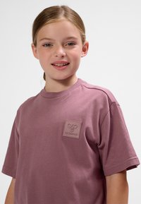 Ledig, kortärmad t-shirt i dammig rosafärg; mjuk bomull med ett strukturerat logopatch på vänster bröst. Mjuk tygstruktur.