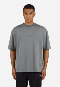 T-shirt din bumbac gri, cu mâneci scurte, gât rotund și logo-ul "PEGADOR" imprimat în gri închis contrastant în centru.