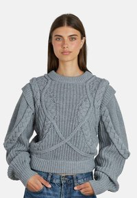 Grau gestrickter Pullover mit strukturierten Zopfmustern, überschnittenen Schultern und gerippten Bündchen. Leichter Stoff mit lockerer Passform.