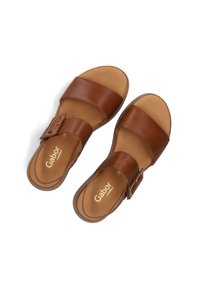 Bruine leren sandalen met twee brede banden en een haaksluiting aan de zijkant. De binnenzolen zijn bruin en hebben de merknaam "Gabor" in het goud. Plat zoolontwerp.