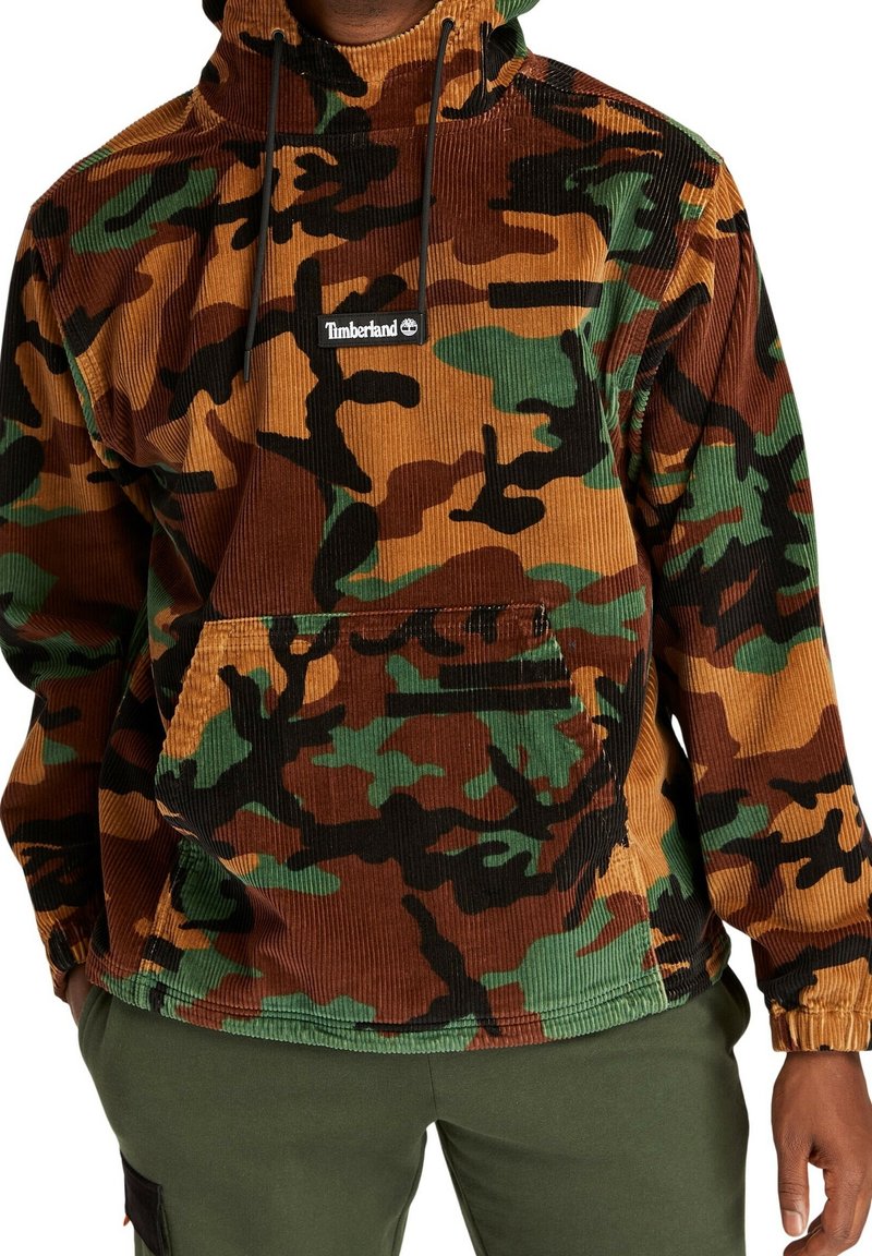 Pull-over en velours côtelé avec un motif camouflage marron, vert et noir, doté d'une poche ventrale et d'un logo Timberland. Capuche réglable.
