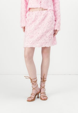 Set di vestito e gonna rosa realizzato in tessuto con texture a rosa. Abbinato a sandali con tacco alto beige con lacci alla caviglia.