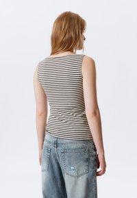 Top sem mangas riscado em bege e castanho escuro, design ajustado, textura suave, combinado com jeans de denim azul claro, soltos, com detalhes desfiados.
