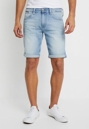 Jasnoniebieskie szorty dżinsowe z podwiniętymi mankietami, pięciokieszeniowym krojem oraz delikatnym wzorem w stylu spranego denimu. Noszone z białymi trampkami.