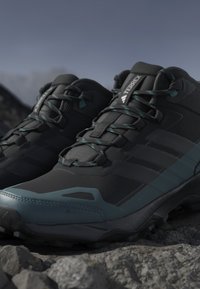 Sorte vandresko med turkise accenter, der har en tekstureret overflade, et sikkert snøresystem og robuste s�åler for godt greb på ujævnt terræn.