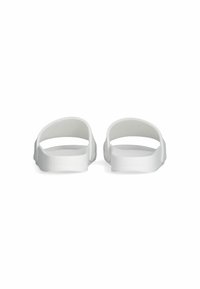 White slide sandals featuring a flat sole, open back, and two rounded straps. Smooth texture with a slight sheen. Simple design, no embellishments.