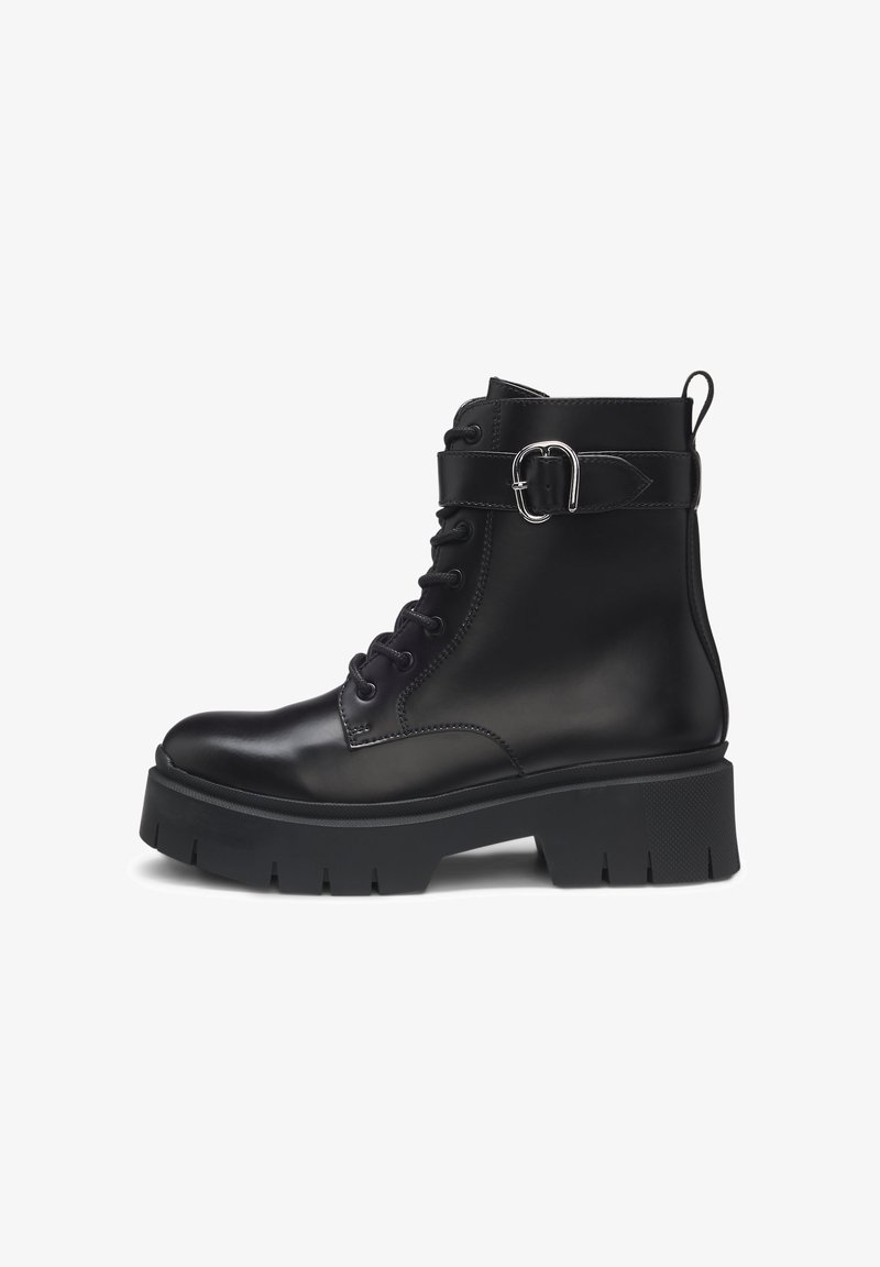 Bottine noire en cuir avec semelle épaisse à crampons, fermeture à lacets à l’avant et bride décorative à boucle argentée autour du haut.