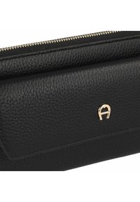 Bolso de cuero negro con superficie texturizada, que presenta un acento del logo en dorado y un cierre de cremallera en la parte superior. Diseño compacto y rectangular.