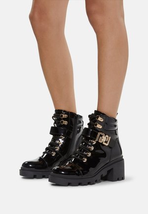 Black patent leather ankle boots with a chunky heel, featuring gold hardware, lace-up front, and a side zipper for closure.