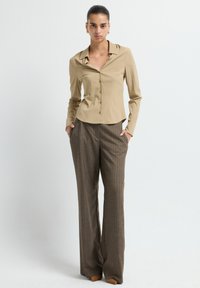 Camicia beige con colletto pieghevole abbinata a pantaloni marroni a righe sottili, con una vestibilità su misura e una texture liscia.