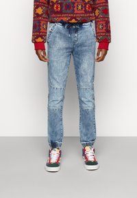 Svetle modré denimové jogger kalhoty s elastickým pasem a manžetami. Mají panelový design s vybledlým praním a bočními kapsami.