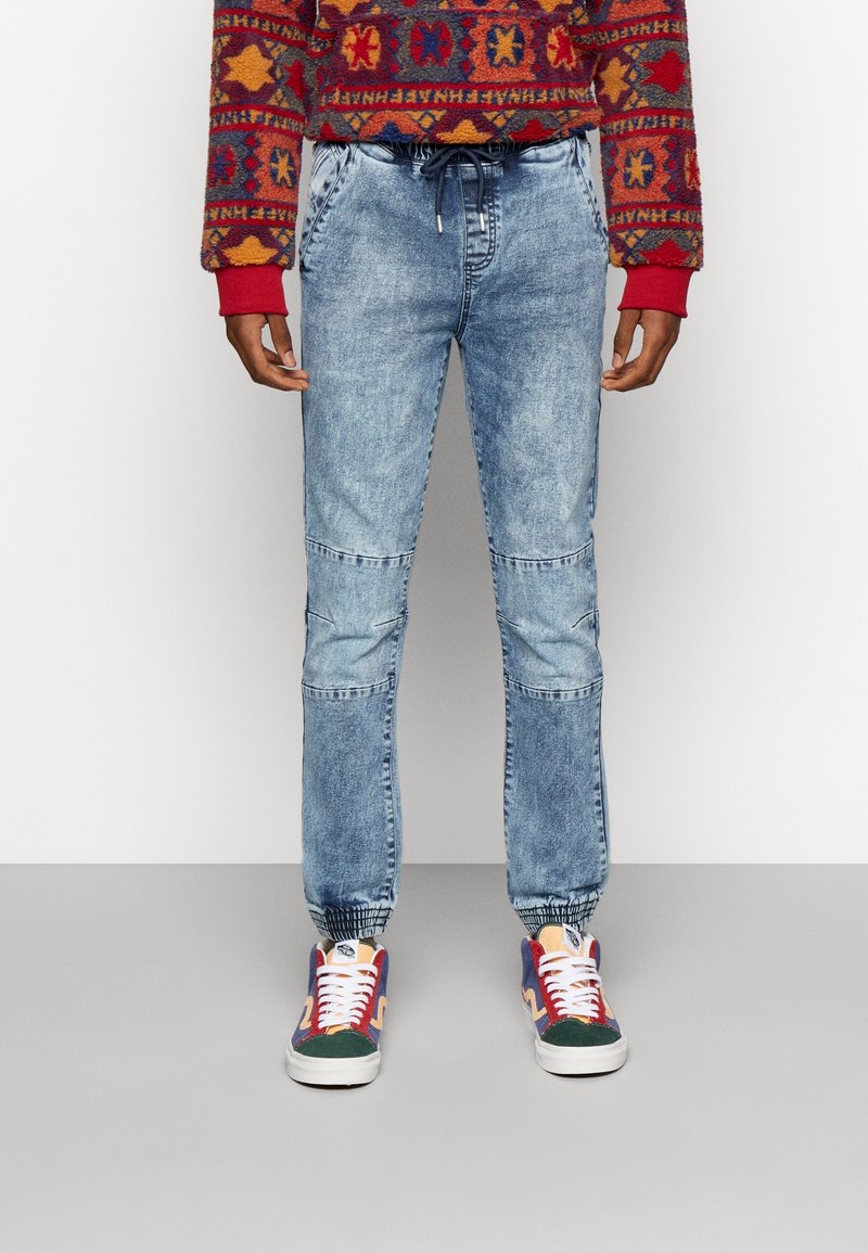 Svetle modré denimové jogger kalhoty s elastickým pasem a manžetami. Mají panelový design s vybledlým praním a bočními kapsami.