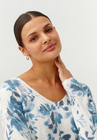 Sweter w kwiaty z dekoltem w serek, z białą bazą i niebieskimi wzorami kwiatowymi. Miękka, dziana struktura z długimi rękawami.