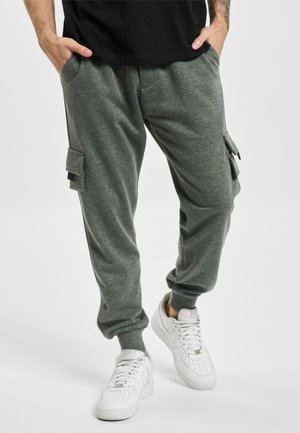 Grå sweatpants med sidelommer, ribbede mansjetter og en myk tekstur. Kombinert med hvite sneakers og en svart t-skjorte.