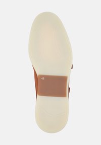 Scarpa in suede marrone con suola in gomma bianca; presenta una toppa rettangolare di un marrone medio con l'etichetta "43" per la taglia. Texture complessivamente liscia.
