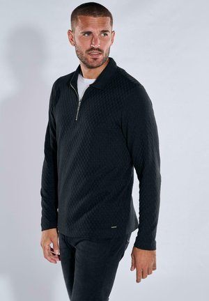 Black zip-up pullover with a textured pattern, long sleeves, and a collar. Features a silver zipper and a small accent logo at the hem.