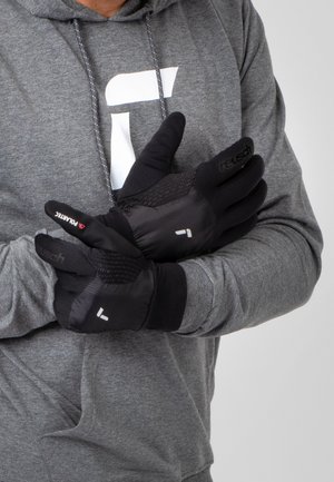 Schwarze isolierte Handschuhe mit strukturierten Handflächen und Fingern, die ein Logo und rote Akzente aufweisen. Getragen von einer Person in einem grauen Kapuzenpullover.