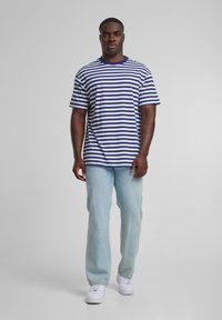 T-shirt rayé bleu marine et blanc avec un col rond, associé à un jean droit bleu clair et des baskets blanches.