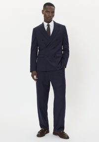 Mornarčki odijelo s dvostrukim kopčanjem i reverom, odgovarajuće hlače, i bijela košulja, upotpunjeni uskim crnim kravatom i smešim cipelama.