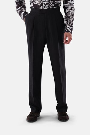 Mann trägt schwarze plissierte Hose mit Seitentaschen, kombiniert mit einem schwarz-weißen, blumigen Langarmhemd und dunkelbraunen Mokassins.