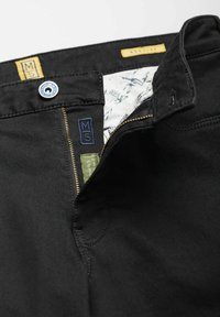 Pantalon noir avec une fermeture éclair visible, un bouton de fermeture et une étiquette de poche cousue. L'intérieur présente une doublure à motifs et des étiquettes supplémentaires.