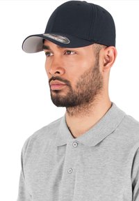 Marine baseballpet met een grijze klep, gemaakt van zachte stof, voorzien van stikselaccenten en een platte klep. Draagt bij een lichtgrijze polo.