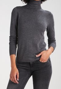 Grauer Rollkragenpullover aus einem weichen Stoff, mit langen Ärmeln und gerippten Bündchen, kombiniert mit dunkelgrauen Jeans.