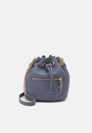 Petit sac seau en cuir bleu avec bandoulière chaîne dorée, fermeture à cordon et poche zippée à l’avant.