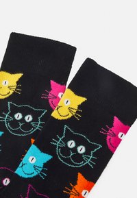 Colorful cat-patterned socks on a black background. Features yellow, pink, cyan, and black cat faces with whiskers and large eyes. Cotton blend.