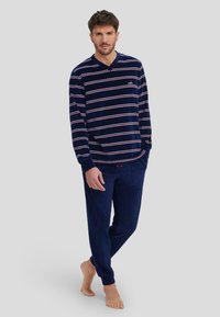 Conjunto de ropa de casa a rayas en azul marino, con una parte superior de manga larga que presenta un escote en V y rayas en blanco y rojo, junto con pantalones a juego de una tela suave y texturizada.