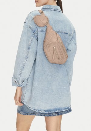 Mujer con chaqueta vaquera azul claro de gran tamaño y bolso beige acolchado cruzado con múltiples bolsillos con cremallera.