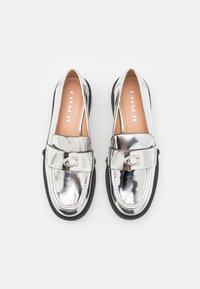 Mocassins en cuir métallisé argent avec des semelles noires, ornés d'une sangle avec un emblème en "C" et "COACH" imprimé sur les semelles intérieures beige.