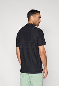 Μαύρο κοντομάνικο πουκάμισο με διακριτικό γεωμετρικό μοτίβο, με στρογγυλή λαιμόκοψη και άνετη γραμμή, απεικονίζεται από πίσω.