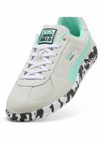 Lys grå ruskinds sneaker med mintgrønne detaljer, hvide snørebånd og en struktureret sål med sort-hvide mønstre; har et logo patch.