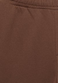 Tissu marron avec une taille élastique et une couture latérale, probablement une partie d’un vêtement comme un pantalon ou une jupe.