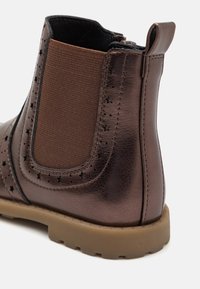 Botín de cuero marrón hasta el tobillo con panel lateral elástico y recortes en forma de estrella, que presenta una ligera suela de goma marrón y un diseño de punta redondeada.