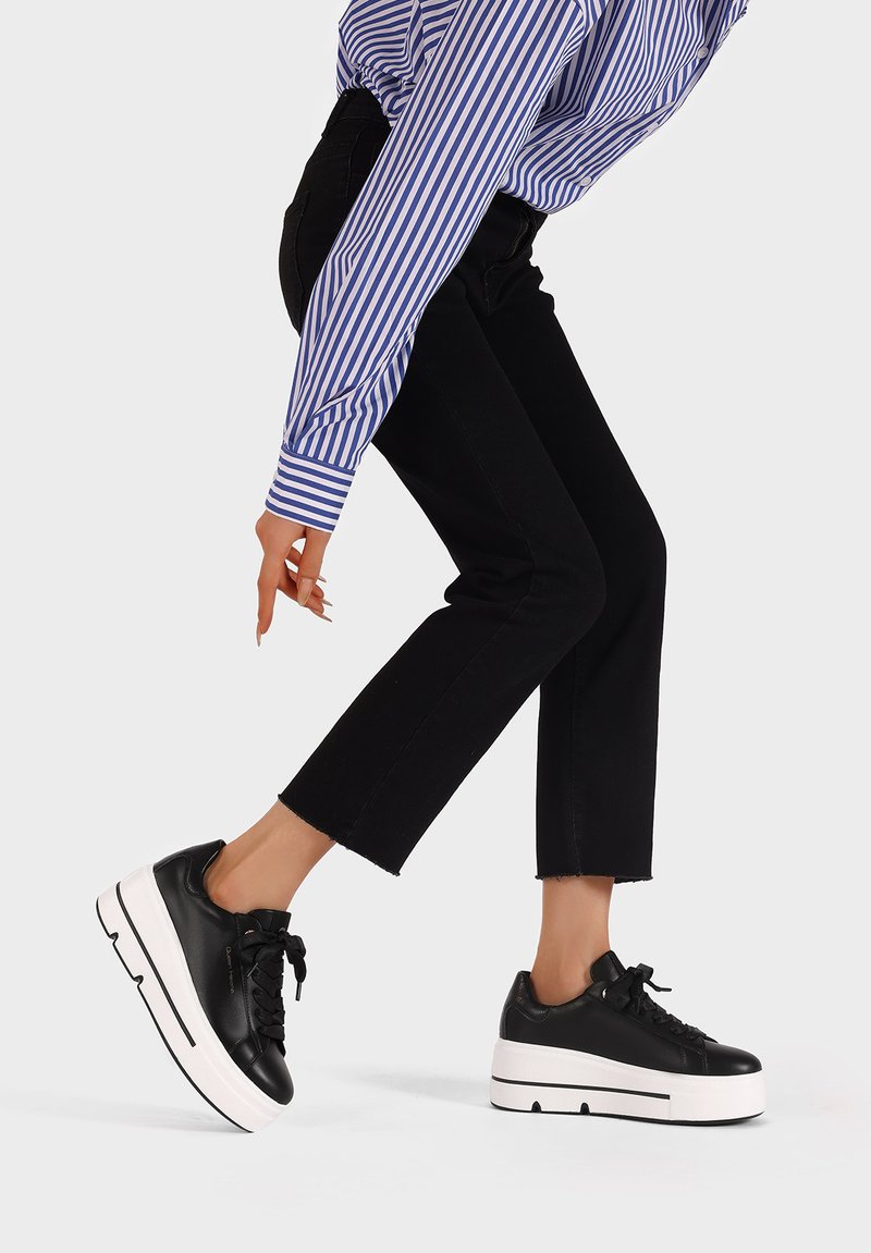 Sneaker platform in pelle nera con suola spessa bianca, dotati di lacci neri e una superficie liscia. Indossati con jeans neri a vita alta.