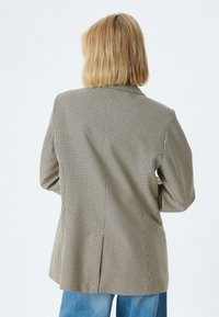 Bruine houndstooth oversized blazer met een enkele split aan de achterkant en brede revers, gecombineerd met lichtblauwe jeans. Getextureerde stof.