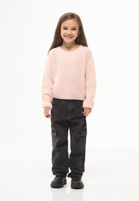 Jasnoróżowy, teksturowany sweter z długimi rękawami, zestawiony z czarnymi spodniami cargo z bocznymi kieszeniami i mankietami. Czarne buty.