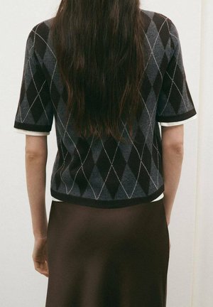 Suéter de manga corta en negro y gris con patrón de rombos y ribete blanco, combinado con una falda de satén marrón, mostrado desde atrás.