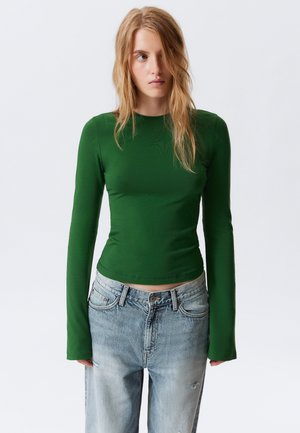 Groene fitted longsleeve top van rekbaar materiaal, gecombineerd met lichtblauwe versleten high-waisted jeans. Minimale ontwerp en naadloze randen.