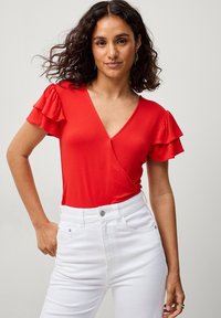 Rode top met korte mouwen, voorzien van ruches, een V-hals ontwerp en een aansluitende pasvorm, gecombineerd met witte high-waisted jeans. Glad textuur.